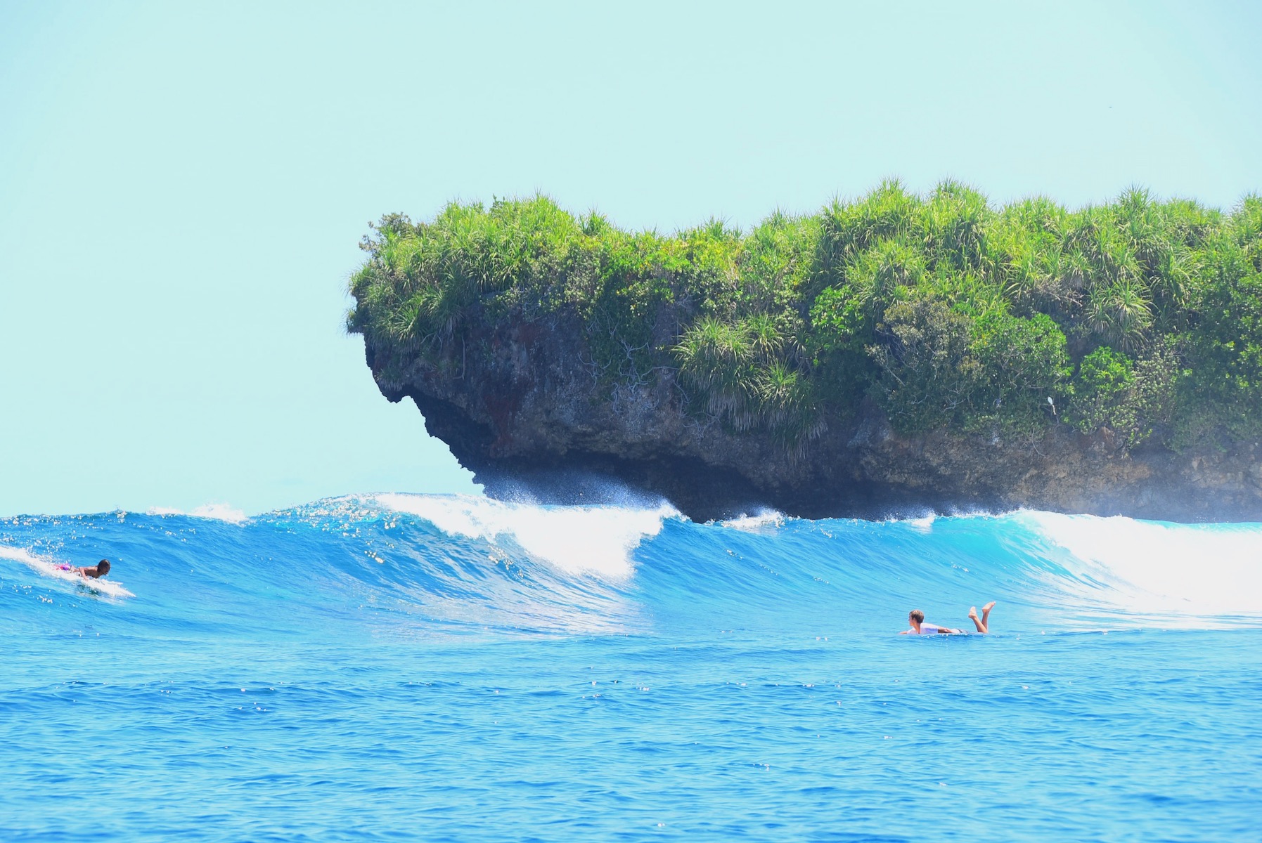 Image of some people surfing a wave beside the Rock island